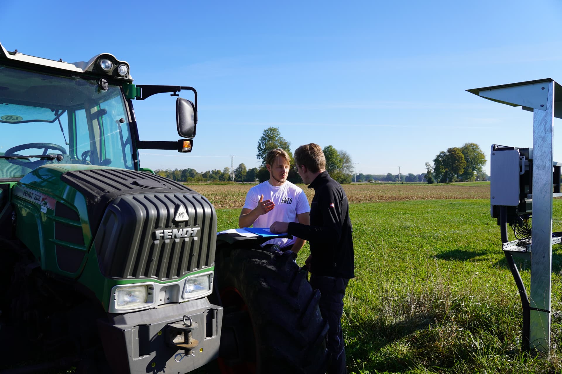 Zwei Eneo-Mitarbeiter im Gespräch am Traktor neben einer Agri-PV-Anlage